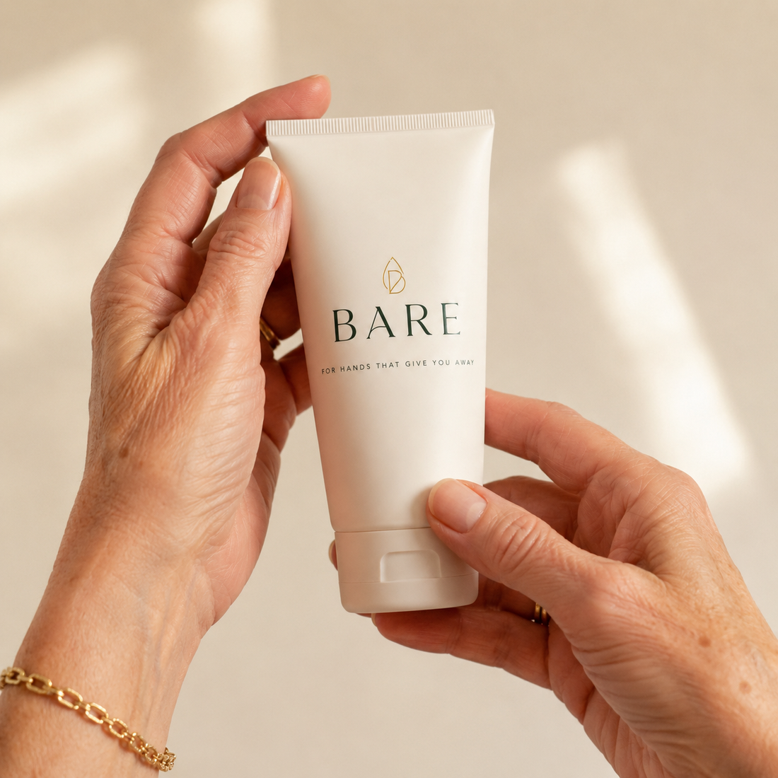 Older hands holding the BARE hand cream tube